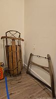 Antique wooden sled standing upright next to wooden frame hand saw against wall