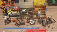 Wide view of assorted power drills, corded and cordless, jigsaw, battery chargers, and various hand tools laid out on the floor.