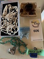 Multiple jewelry pieces arranged on a table, including freshwater pearl strands, jade necklace, amber jewelry in box, and ring with green stone.