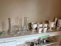Shelf with clear glass bud vases on left, small and medium white ceramic plant pots and planters to the right.