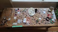 Full assortment of costume jewelry spread on a wooden table showing necklaces, brooches, pins, earrings, bracelets, and packaged small items.