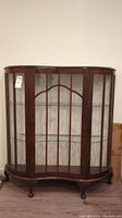 Front view of wooden display cabinet with glass doors and shelves, showing curved front and ornate feet.