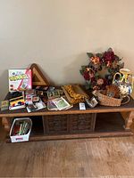 View of game items, flower wreath, ceramic vase, basket, wooden cribbage board, playing cards, and other accessories on a wooden TV stand.
