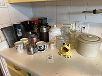 Photo showing entire lot of kitchen items including Braun coffee grinder, Melitta coffee pot, canisters, mugs, tea pots and soap dispenser