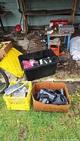 Wide shot showing boxes of assorted hardware fittings, safety vests in a tote bin, a dolly, hand tools in cases, and a red toolbox on a table.
