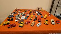 Overview of approximately 40 Matchbox toy cars arranged on an orange surface, showing various models and colors