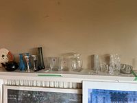 Collection of various glass and crystal items including vases, a teapot, and a handheld fan arranged on a shelf above green tape.
