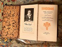 Photo showing book opened to a portrait of John Keats and signed facsimile on left page, title page on right with decorated orange border and floral design, marbled faux leather cover visible.