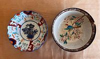 Both antique Japanese porcelain bowls side by side on a wooden surface, showing overall view and visible repair damage.