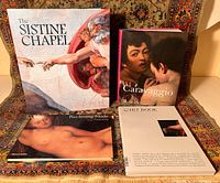 Four art books arranged on patterned backdrop showing covers for The Sistine Chapel, Caravaggio in Detail, Reclining Nude, and the Art Book Quarterly magazine.