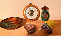 Full lot view: barometer, enamel bowl, beaded bird, tin mirror, piano trinket box on wooden surface