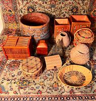 Lot of 12 varied sizes and types of woven and wooden boxes and baskets shown on a patterned rug.