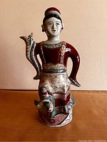 Front angled view of antique Chinese dancing lady ewer with the left arm lowered as handle and right arm raised with spout shaped like a snake or dragon head.