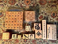 Top-down view of multiple blocks including two plastic-cased sets of Chinese character rubber stamps, smaller individual stamps, and larger calligraphy stamps arranged neatly on a patterned carpet.