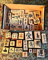 Top-down photo of a box filled with over 20 wooden blocks rubber stamps with Chinese characters on at least one side, arranged in rows showing details of characters.