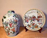 Front view of ginger jar beside decorative plate on a wooden surface against a plain background.