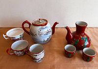 Wide view showing Japanese Kutani porcelain teapot, two matching Kutani sake cups, two matching porcelain tea cups, and one English china tea cup with chip.