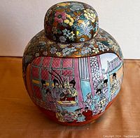 Front view of the round porcelain ginger jar with painted traditional scene of people and floral patterns with gold accents on lid and upper body