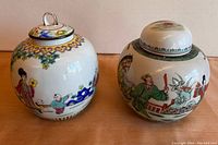 Photo of two porcelain ginger jars with lids showing hand-painted traditional Asian scenes and decorative patterns