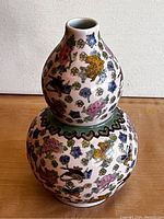 Front view of Chinese porcelain gourd vase showing detailed hand-painted flowers, birds, and butterflies with a narrow neck and green scalloped band.