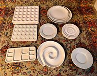 Top view of all porcelain mixing trays and plates arranged on a patterned carpet, showing various sizes and designs, white porcelain, clean condition.
