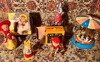 Group shot of five vintage tin wind-up toys on patterned carpet including two in original boxes plus figures of rabbit, clown, duck on bike, and child riding animal toy.