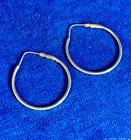 Pair of round yellow gold hoop earrings on blue fabric background.