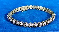 Photo of silver tennis bracelet with pink spinel stones set in heart-shaped links, displayed on blue fabric background.