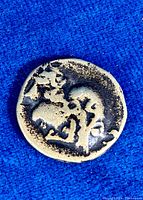 Top-down photo showing the coin on blue fabric background highlighting the obverse with a human/deity profile figure.
