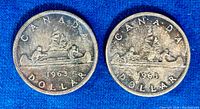 Two Canadian silver dollar coins from 1963 shown side by side, displaying the canoe paddle design, with 'CANADA DOLLAR' and year 1963 inscriptions.