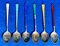 Set of six sterling silver teaspoons displayed in a row on blue fabric, each with different colored guilloche enamel handles.