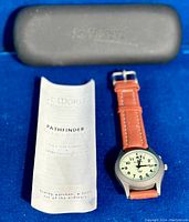 St Moritz branded black carrying case, operating instructions for Pathfinder titanium alarm watch, and the watch displayed on blue fabric background.