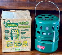 Overall view of the green Coleman Model 510A catalytic radiant heater next to its original cardboard box with branding and usage instructions.