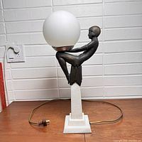 Front view of entire lamp on marble base with bronze-tone metal figure holding frosted globe.