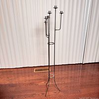 Front view of tall metal floor-standing candle holder with five arms and tripod base.