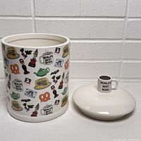 Cookie jar with lid removed showing illustrations on the body and separate lid with mug handle