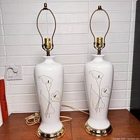 Pair of white ceramic table lamps with brass base and fittings standing side by side showing full height and shape.