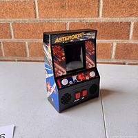 Front angle view of vintage Asteroids arcade game miniature unit on table with brick wall background.