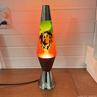Vintage Bob Marley lava lamp turned on showing colorful multi wax blobs in red, yellow, and green. Image of Bob Marley on glass with metallic base and black bottom section with Bob Marley logo.