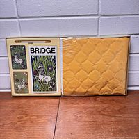 View of the full set in packaging showing playing cards box, score pad, and yellow quilted tablecloth
