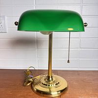 Front view of vintage bankers lamp holding green glass shade, brass base, and pull chain under shade.