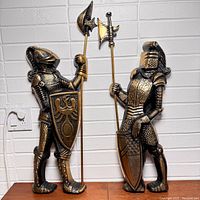 Pair of vintage metal knight wall sculptures standing next to each other, showing full front sides with detailed armor, weapons, and shields.