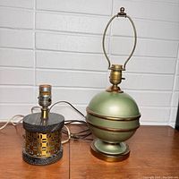 Two vintage lamps shown unlit: ball-shaped green and bronze lamp about 16 inches tall with harp, and smaller black and bronze metal cutout cylindrical lamp without bulb