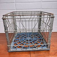 Full view of the square metal wire milk crate with blue plastic base showing age and wear