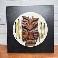 Front view showing carved wood owl on abstract vinyl backing with circular white and colored line design.