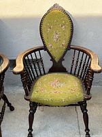 Front view of an antique wooden armchair with light green embroidered fabric upholstery featuring floral patterns on backrest and seat, showing turned wood spindles and armrests.