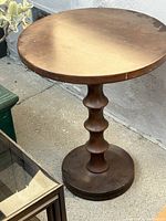 Full view of 26-inch round wooden side table with sculpted pedestal base, showing surface wear and scratches on the tabletop.