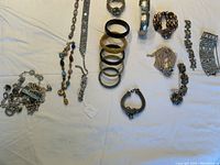Top view showing multiple bracelets and miscellaneous parts laid out on a white surface. Displays variety of styles including bangles and chain bracelets.