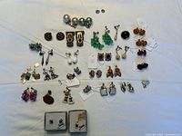 Wide view of the collection of clip-on earrings laid flat on white surface showing various colors and styles including pearl, bead clusters, floral and geometric designs along with two sets in white boxes.