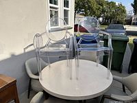 Set of two clear acrylic ghost chairs placed on a white round table, showing front view with armrests and rounded backs